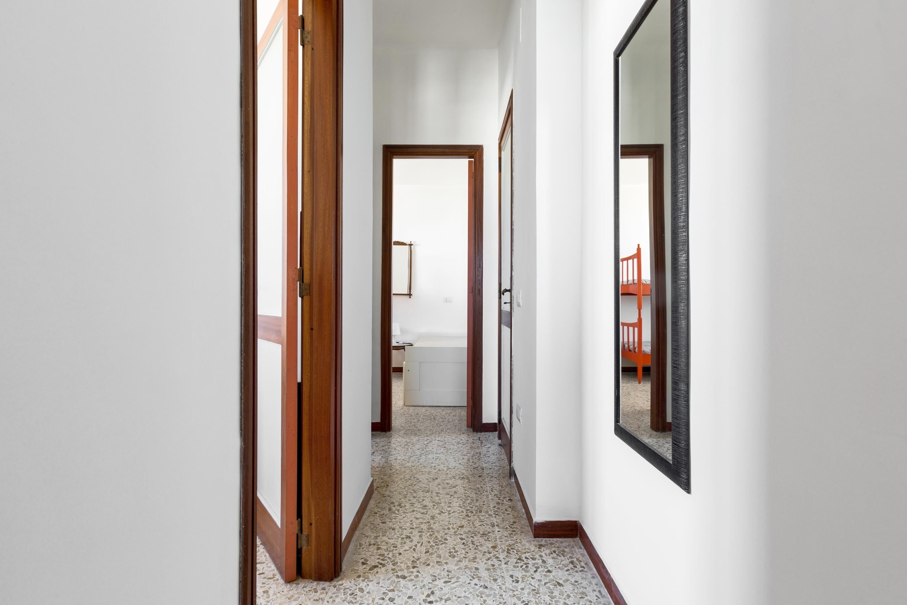 A hallway with a tiled floor, wooden doors, and a large mirror on the right wall.