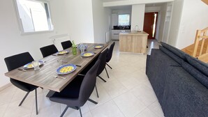 Un espace repas moderne avec une table en bois, des chaises noires et un canapé gris. On aperçoit une cuisine à l’arrière-plan.