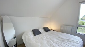 Une chambre avec un grand lit, deux oreillers, une table de chevet avec une lampe, un radiateur et une fenêtre donnant sur un paysage verdoyant.