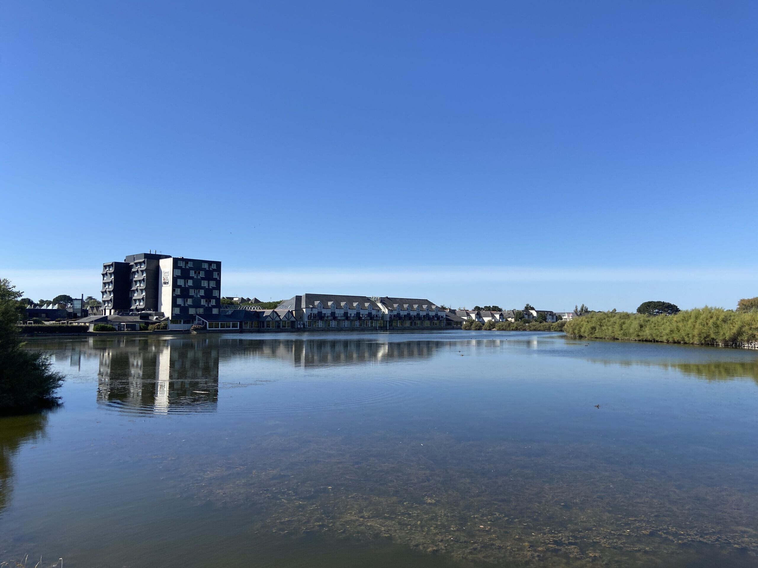 A calm lake with a reflection of buildings, including a tall apartment building and several houses.