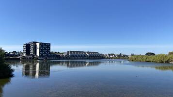 Un lac paisible dont les eaux reflètent les bâtiments environnants, notamment un grand immeuble d’appartements et plusieurs maisons.