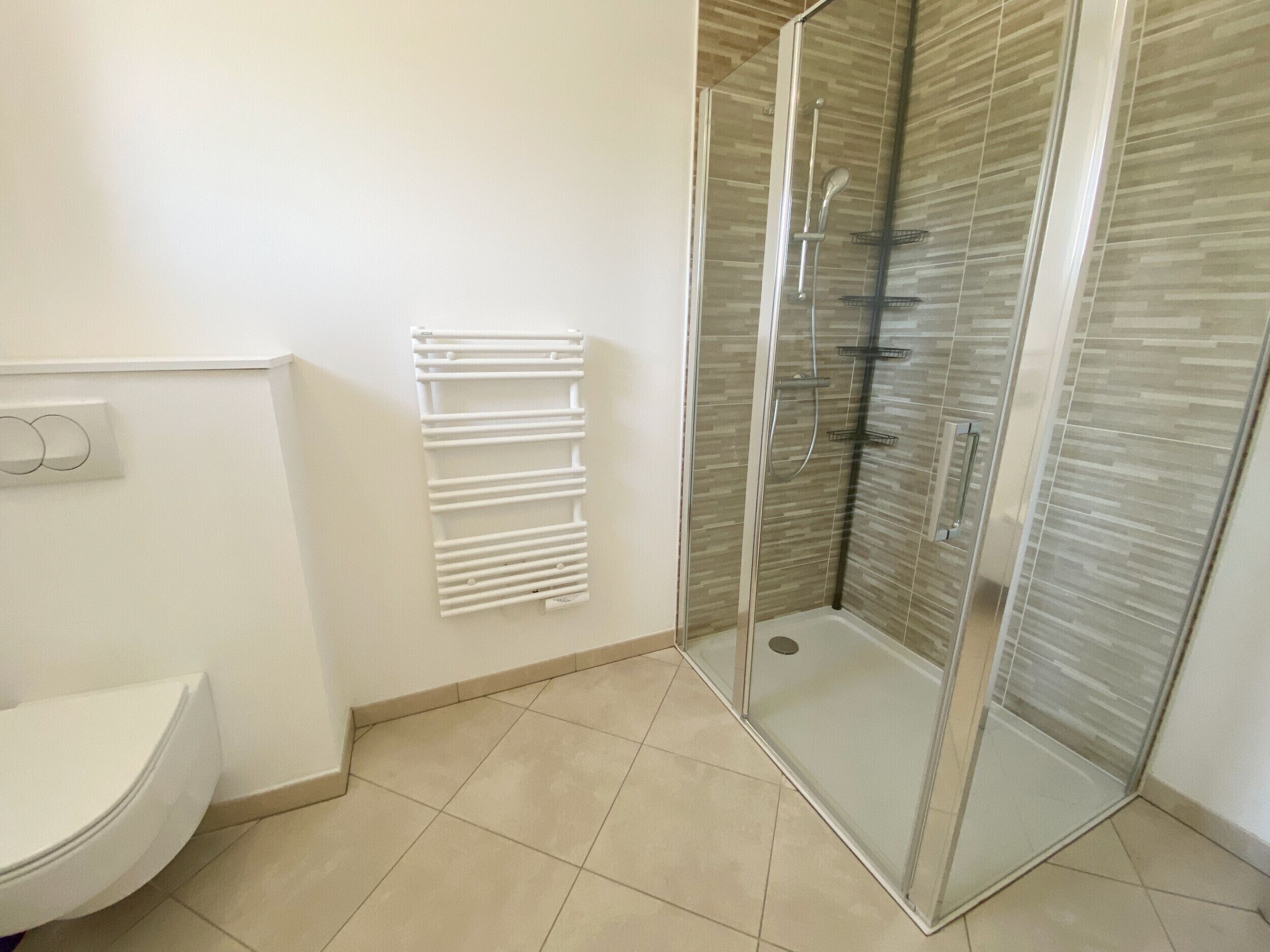 Une salle de bain comprenant des toilettes, une douche à parois de verre et un porte-serviettes blanc.