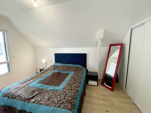 Une chambre à coucher comprenant un lit, une table de chevet, une lampe, un miroir et une armoire.