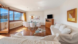 A modern living room with a sofa, a glass coffee table, a dining area with chairs, a TV, and artwork on the walls. - Comfort Holiday In Paradiso With Lake Lugano View (Paradiso)
