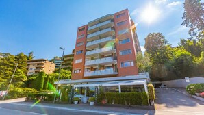 A multi-story hotel with balconies, a covered entrance, and a parking area. - Comfort Holiday In Paradiso With Lake Lugano View (Paradiso)