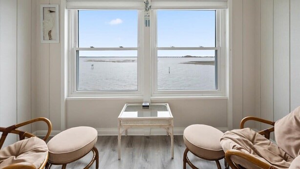 A room with a large window, wicker chairs, a small table, and a framed picture on the wall. - Nicely Renovated Bayfront Condo with Great Sunsets (Ocean City)