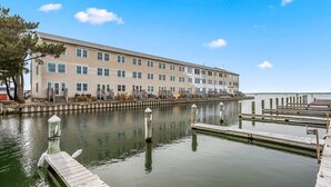 A multi-story building with a dock extending into a calm body of water. - Nicely Renovated Bayfront Condo with Great Sunsets (Ocean City)