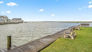A waterfront property with a wooden dock, grassy areas, and a row of houses. - Nicely Renovated Bayfront Condo with Great Sunsets (Ocean City)