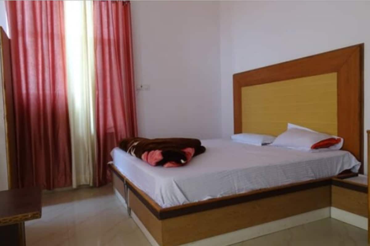 A single bed with a wooden headboard, a bedside table, and a red curtain.
