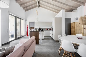 Una cocina moderna con armarios blancos, un comedor con mesa y sillas blancas, y un ventanal que proporciona luz natural.