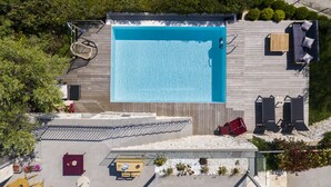 Eine Vogelperspektive auf einen Poolbereich auf einem Dach, mit Schwimmbecken, Liegestühlen, einem Holzterrasse und umgebender Bepflanzung.