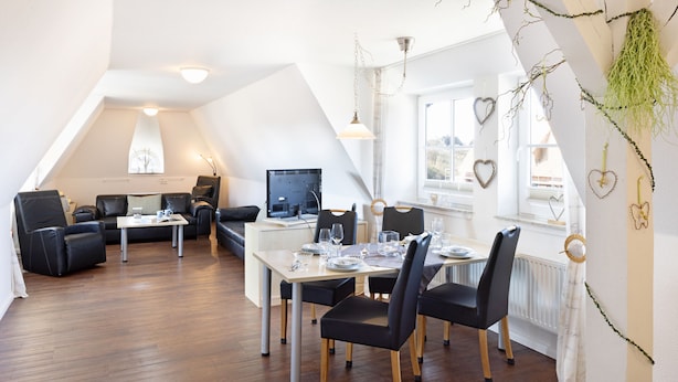 A modern dining area with a long table, black chairs, and a computer monitor on a desk. - Herzlich Willkommen im Appartement Meier (List auf Sylt)