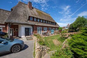 Une maison traditionnelle à toit de chaume, avec une façade en briques, un porche et un mur en pierre.