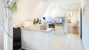 A modern kitchen with white cabinets, a central island, and a dining area. - Herzlich Willkommen im Appartement Meier (List auf Sylt)