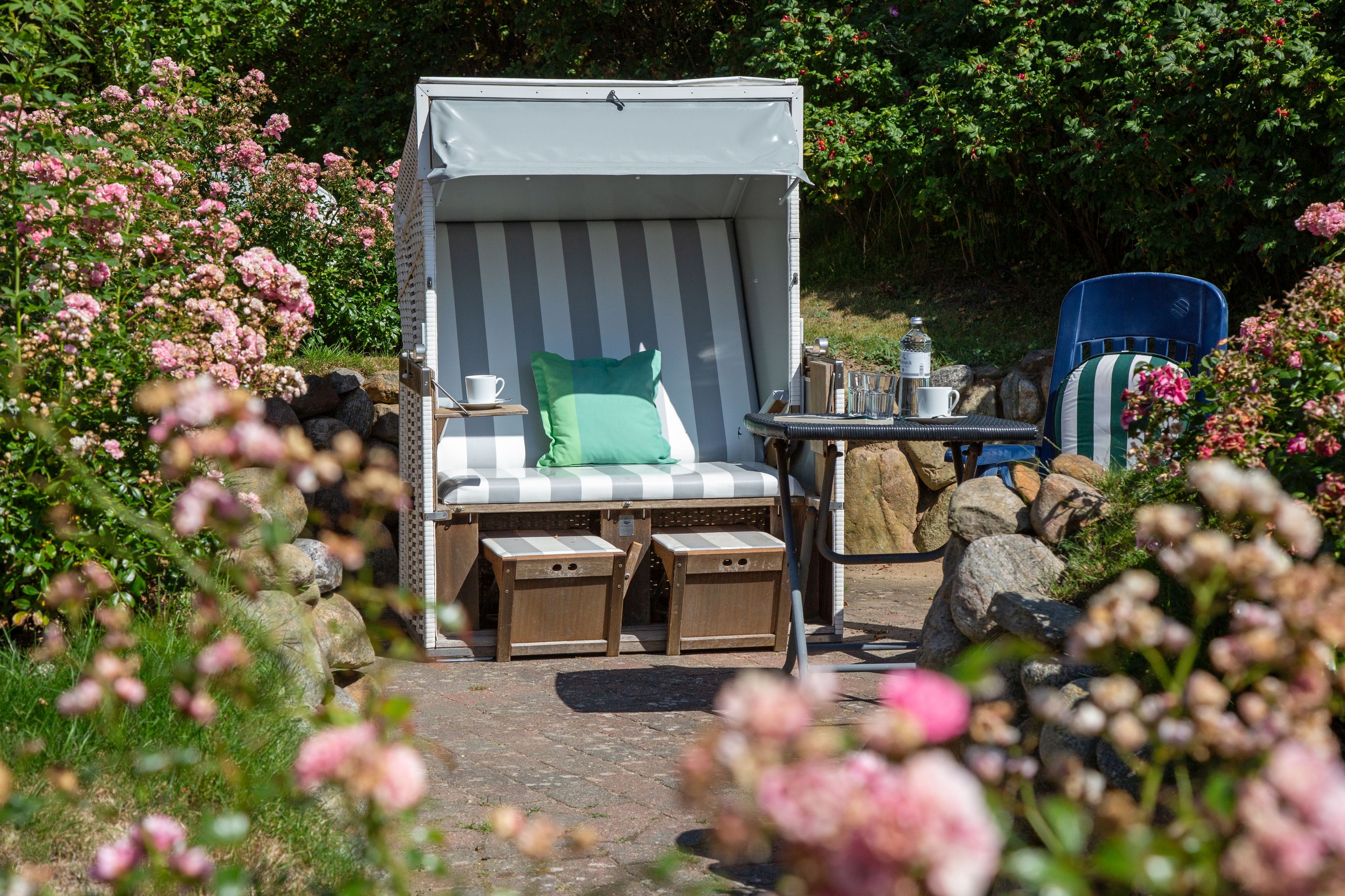 A covered outdoor seating area with a cushioned chair, a table with a water bottle, and a chair with a striped cushion.