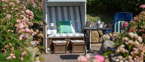 A covered outdoor seating area with a cushioned chair, a table with a water bottle, and a chair with a striped cushion.