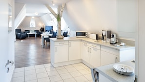 A modern kitchen with white cabinets, a microwave, coffee maker, and a dining area with a table and chairs. - Herzlich Willkommen im Appartement Meier (List auf Sylt)