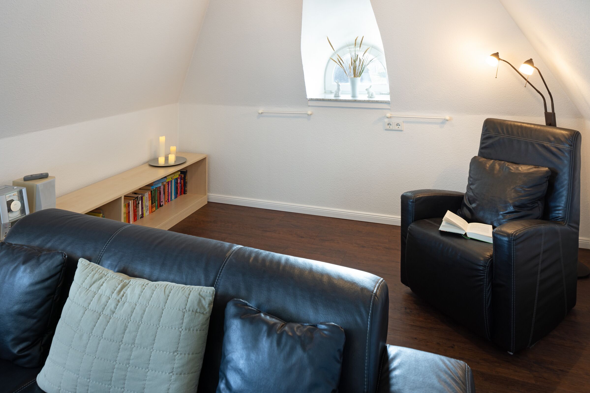 Una sala de estar moderna con un sofá y un sillón de cuero, una estantería y un ventanal con vistas.