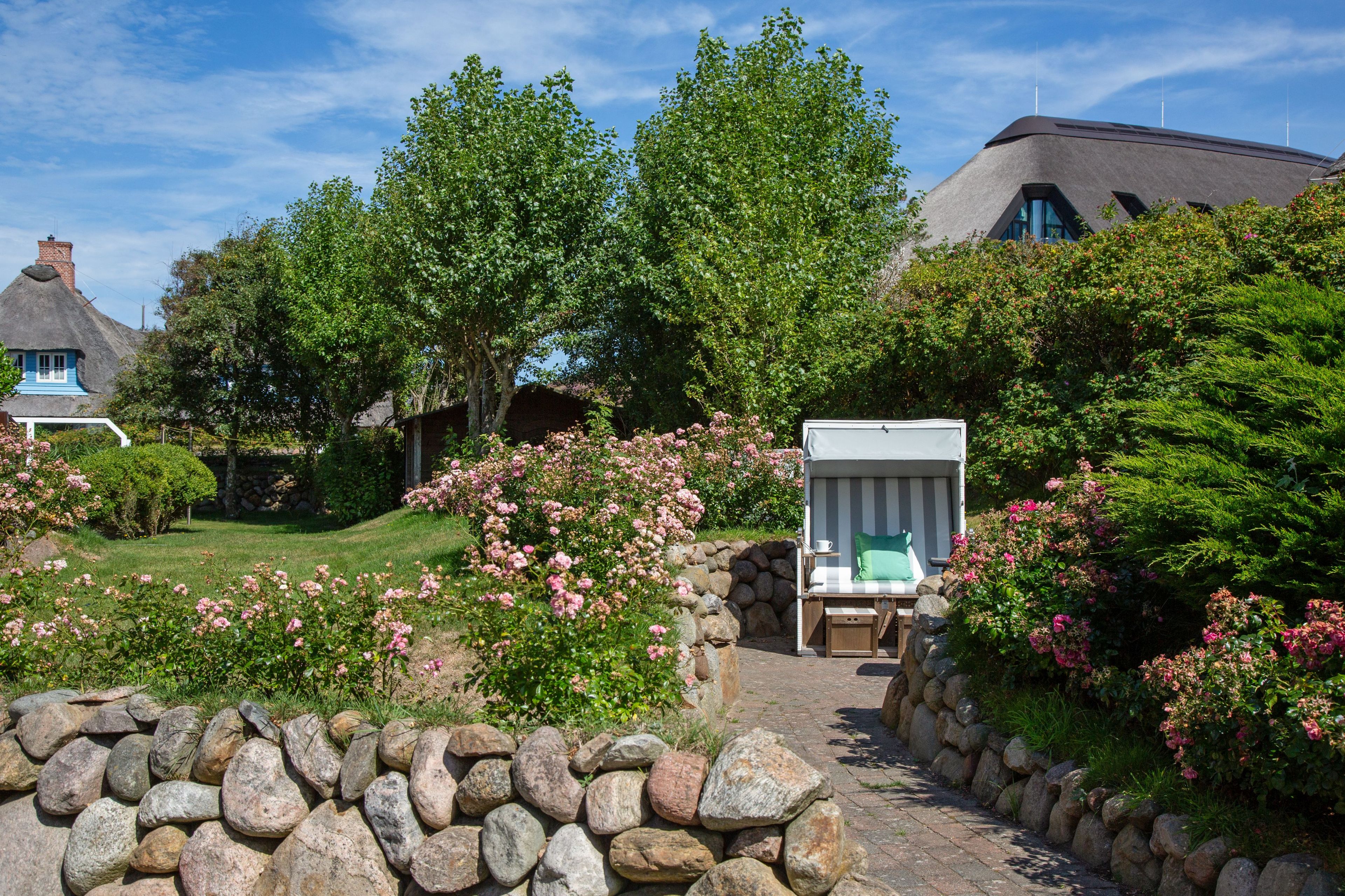 A garden with a stone wall, a thatched-roof cottage, and a modern house with a sloped roof.