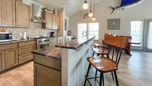 Une cuisine moderne avec des meubles en bois, un plan de travail en granit et des luminaires suspendus.