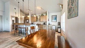 Une cuisine spacieuse avec des meubles en bois, une grande table à manger et des luminaires suspendus.