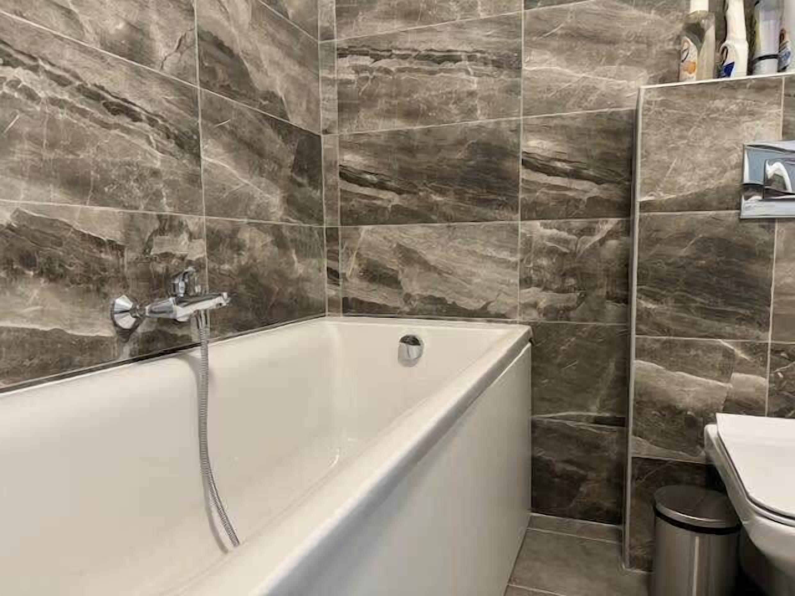 A bathroom with a bathtub, a toilet, and a trash bin.