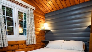 Une chambre dans un chalet en bois, avec un lit, une fenêtre avec des rideaux et une table de chevet avec une lampe.
