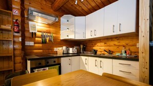 L’intérieur d’un chalet en bois comprend un coin cuisine avec des meubles blancs, une cuisinière et une table à manger.