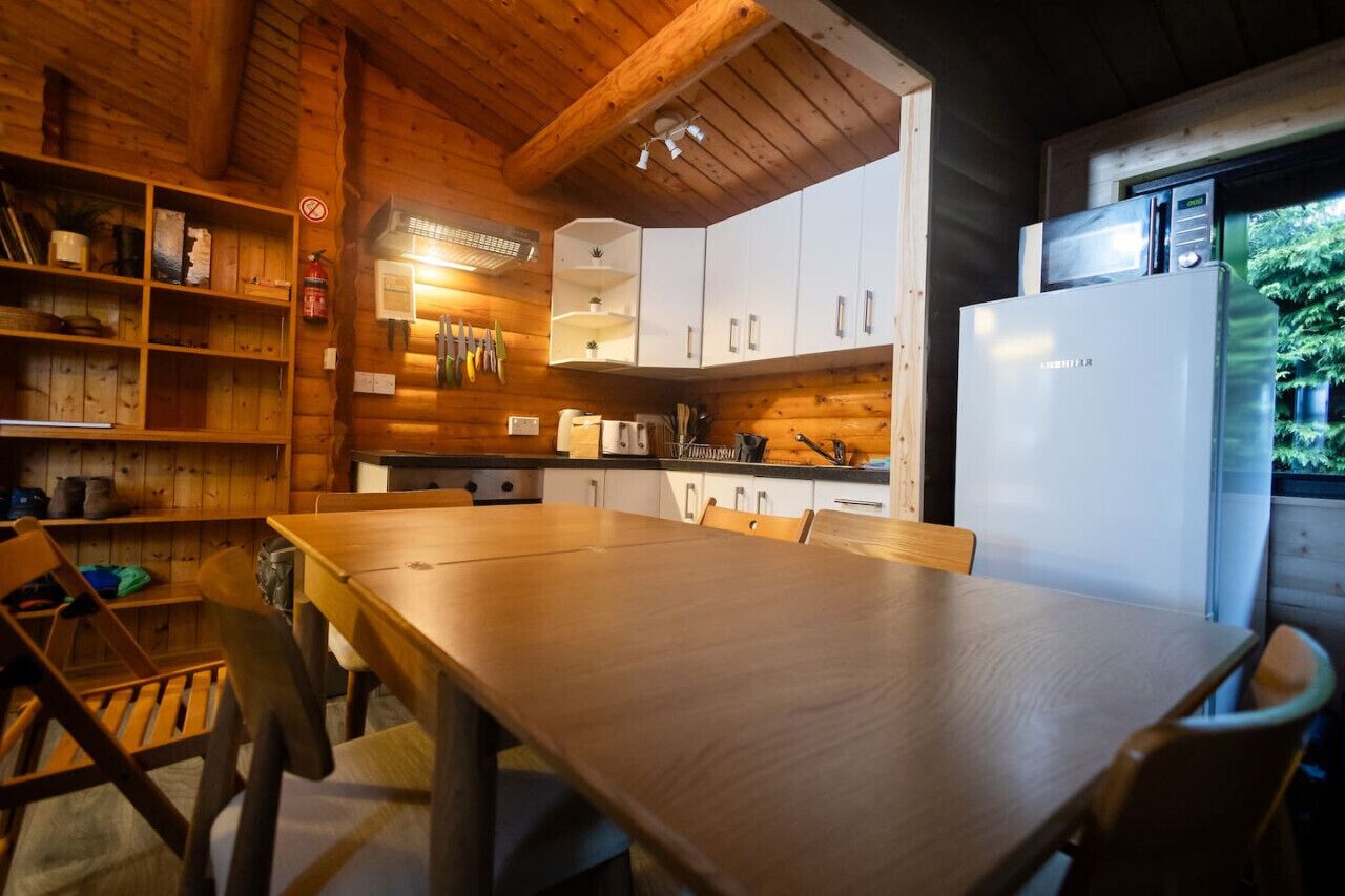 A wooden interior with a dining table, chairs, cabinets, and a refrigerator.