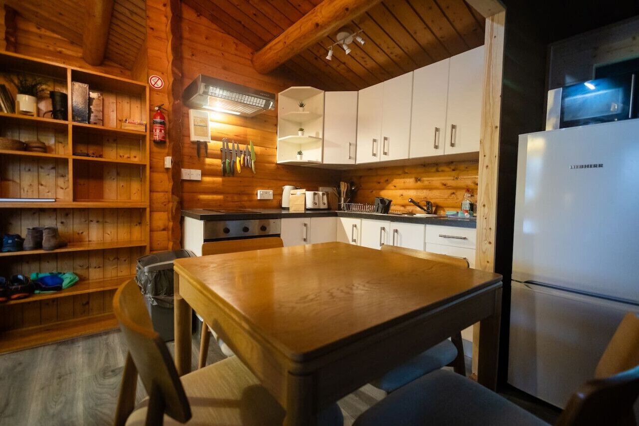 En stuga med träpanel på insidan, ett träbord och stolar, vita skåp, en spis och ett kylskåp.