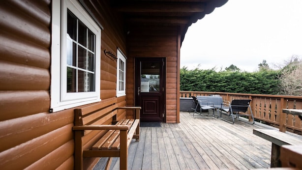 Une terrasse en bois avec des bancs et une porte donnant sur un espace abrité.