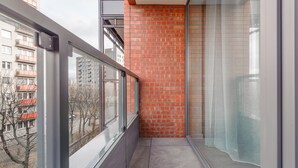 Un balcon étroit avec un mur en briques rouges, une porte vitrée et une vue sur les bâtiments voisins.