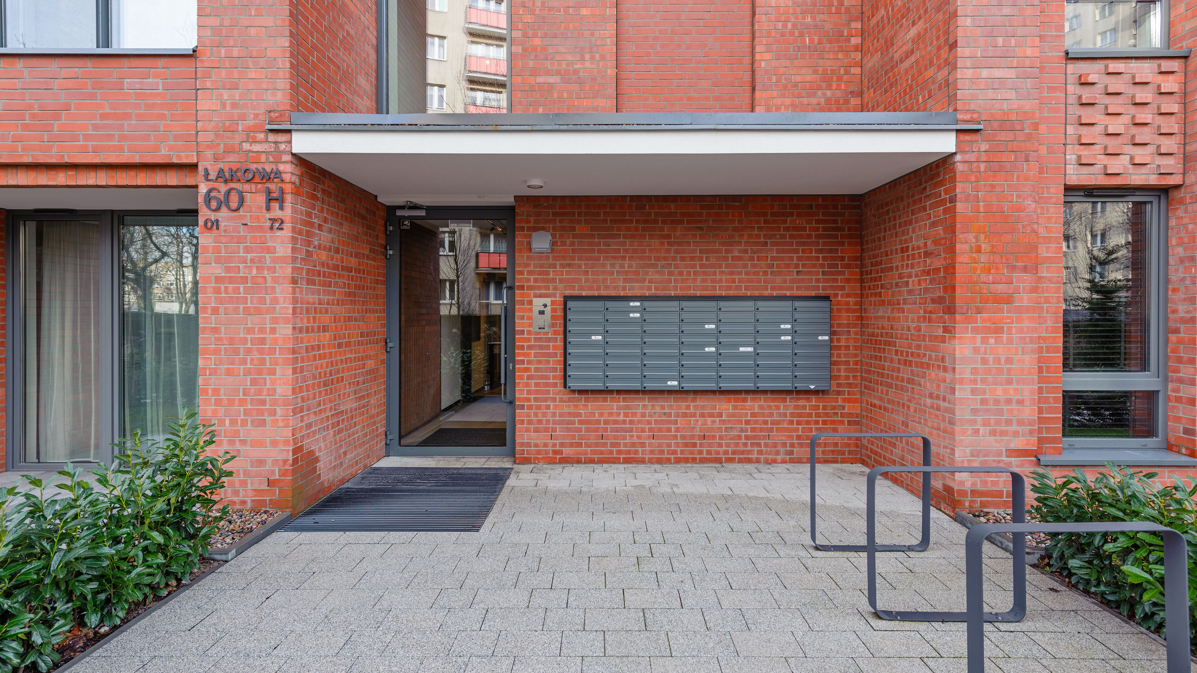 A red brick building with a mailbox, a door, and a small outdoor area with plants.