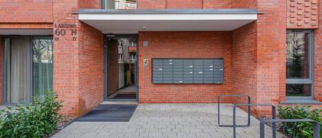 A red brick building with a mailbox, a door, and a small outdoor area with plants.