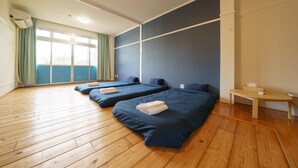 A hotel room with three beds, wooden flooring, a large window with curtains, and a small table with a tissue box. - pension Aloalo (Shirahama)