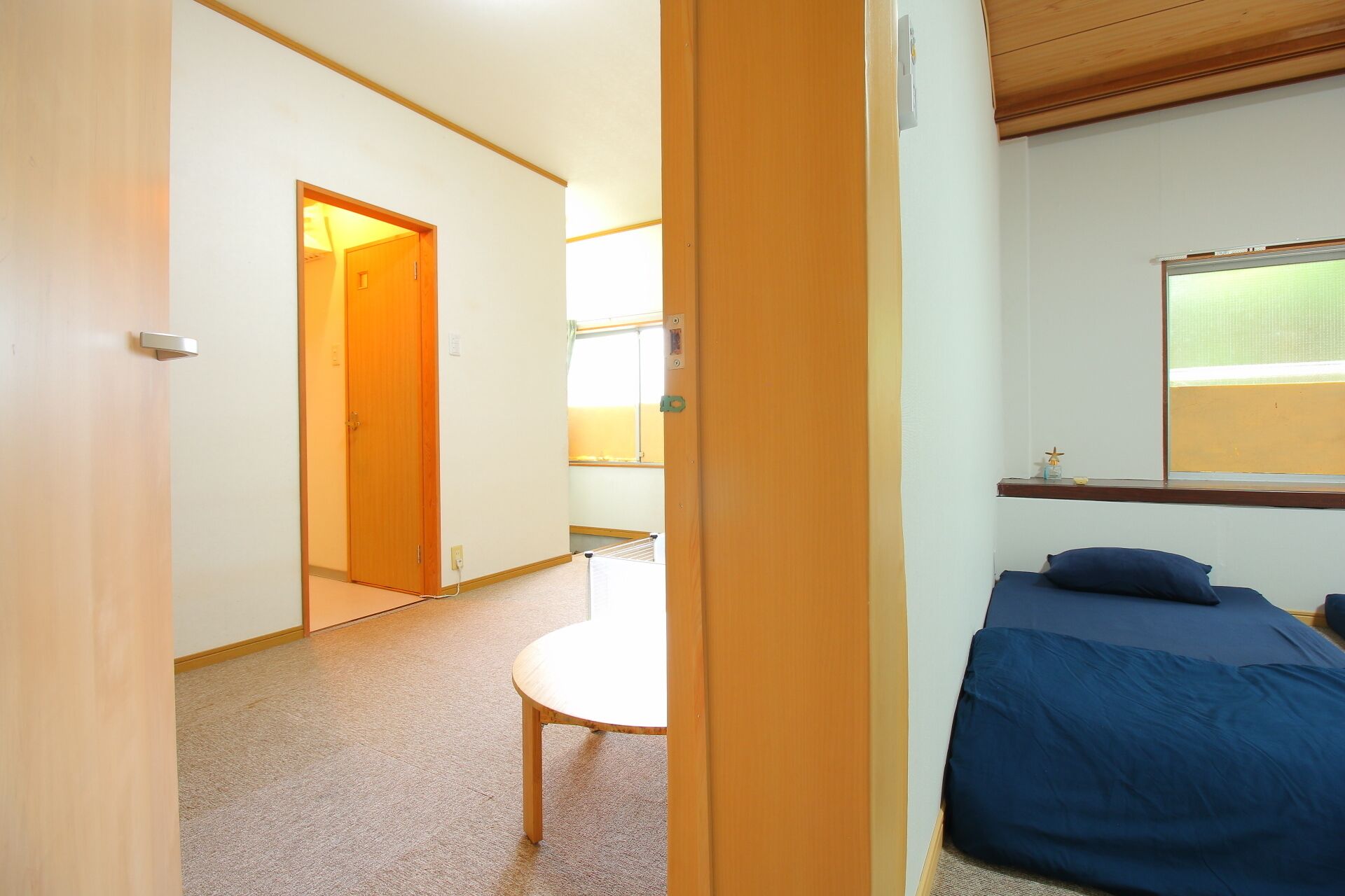 A room with a bed, a small table, and a door leading to another room.