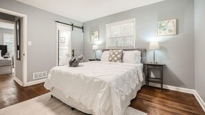 A bedroom with a bed, bedside tables, a window with blinds, and artwork on the walls.
