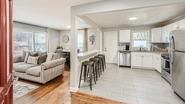 A modern kitchen with white cabinets, a stainless steel refrigerator, and a built-in oven. There is a bar area with stools and a white countertop.