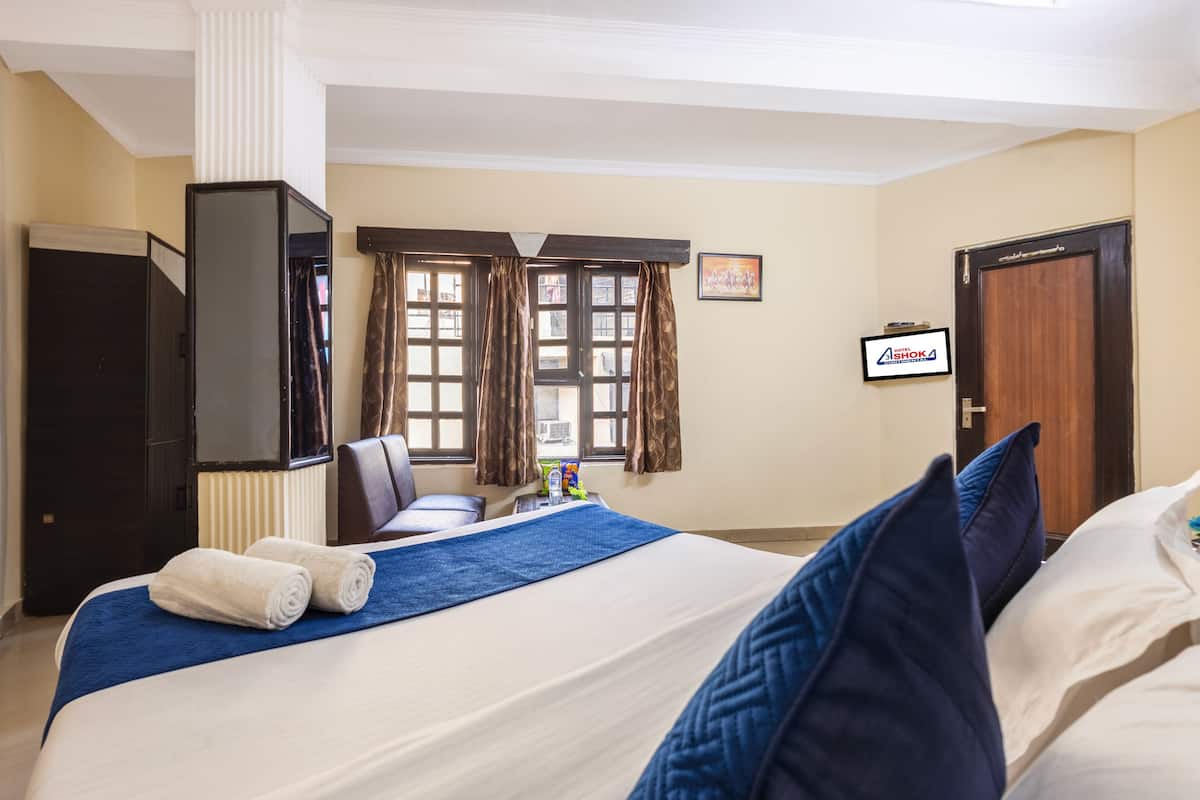 A hotel room with a large bed, a TV, a desk, and a window with curtains.