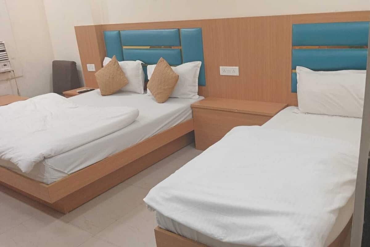 A hotel room with two single beds, each with a wooden headboard and a white mattress.
