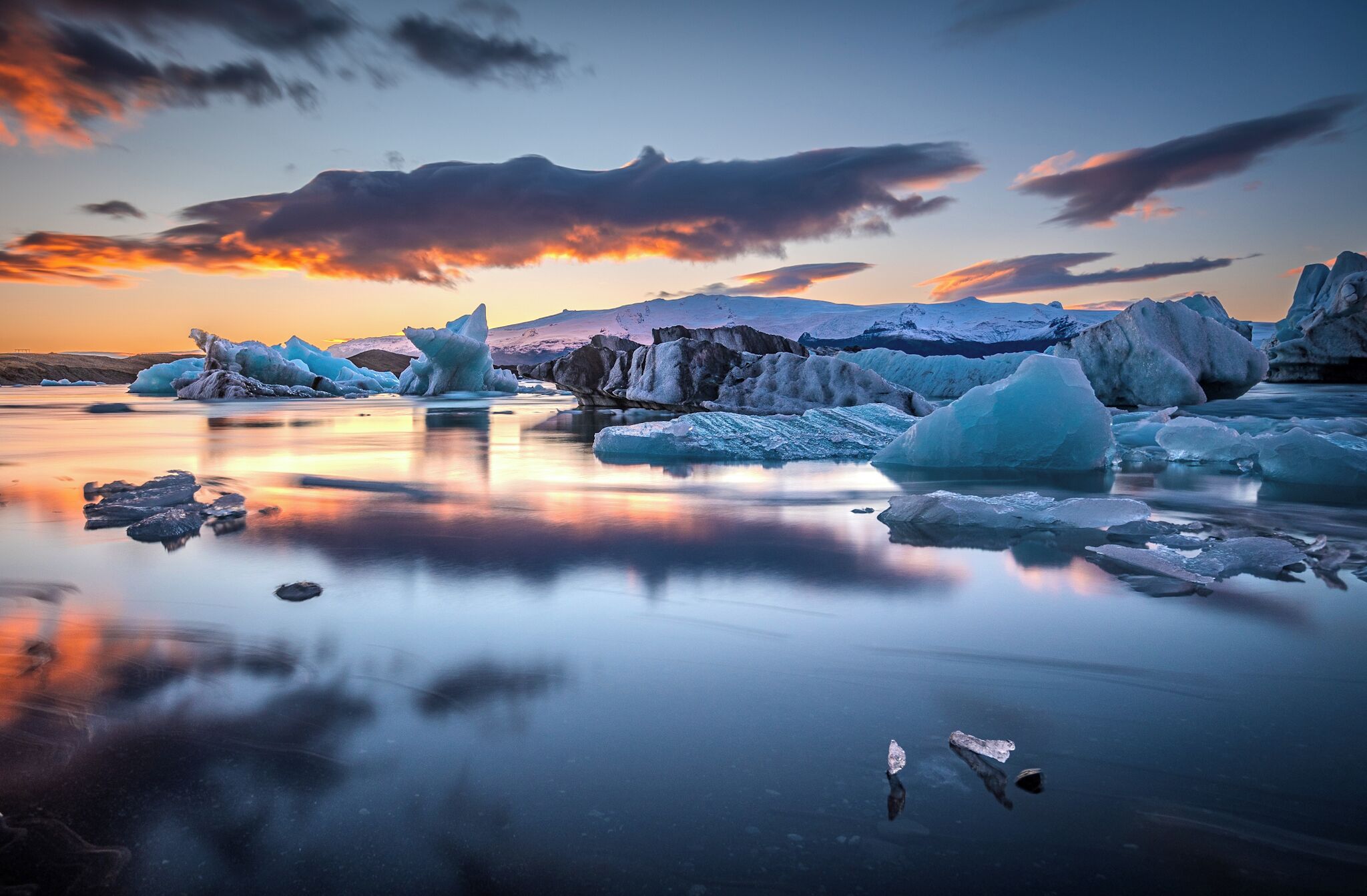 A calm frozen lake with icebergs and a mountain in the background.