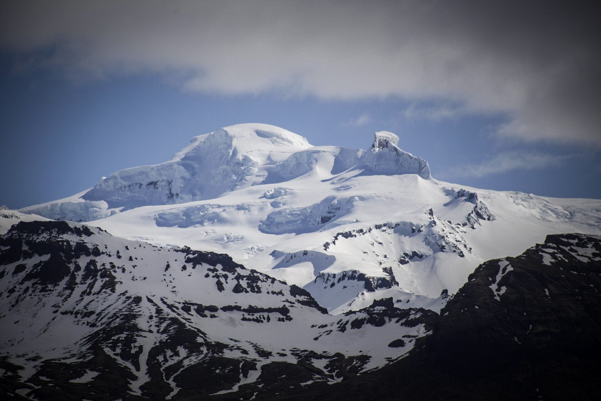 A snow-covered mountain peak with rugged terrain and rocky outcrops.