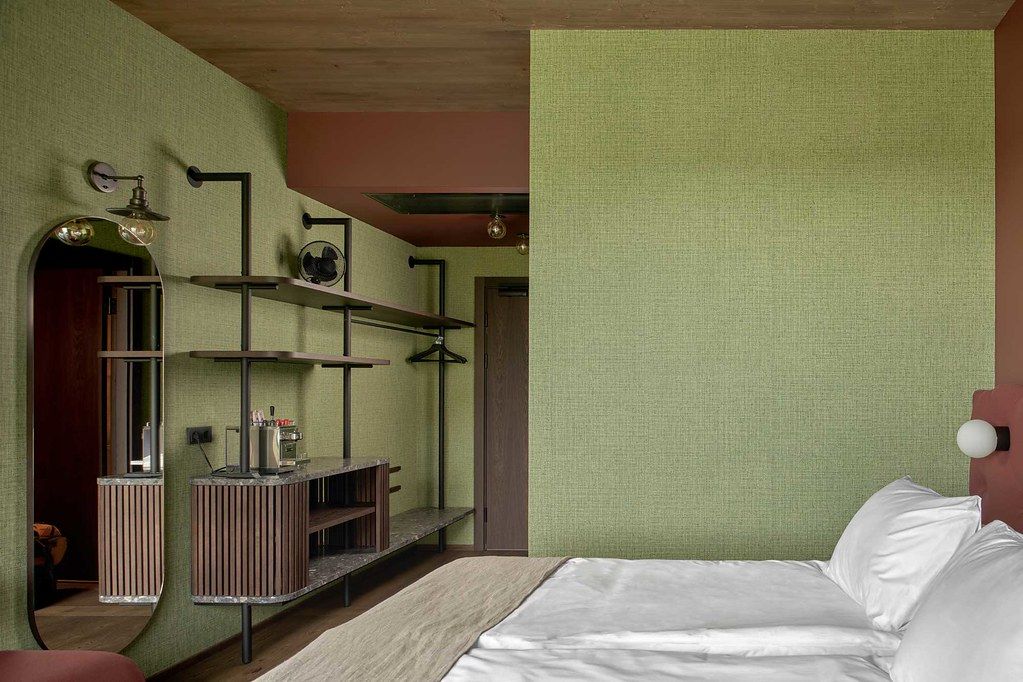 Une chambre à coucher avec un lit, un miroir, une étagère avec des objets et une porte donnant sur une autre pièce.