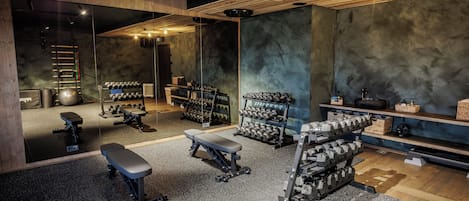 Un gimnasio con diverso equipo de ejercicio, incluyendo mancuernas, bancos y una jaula para sentadillas.