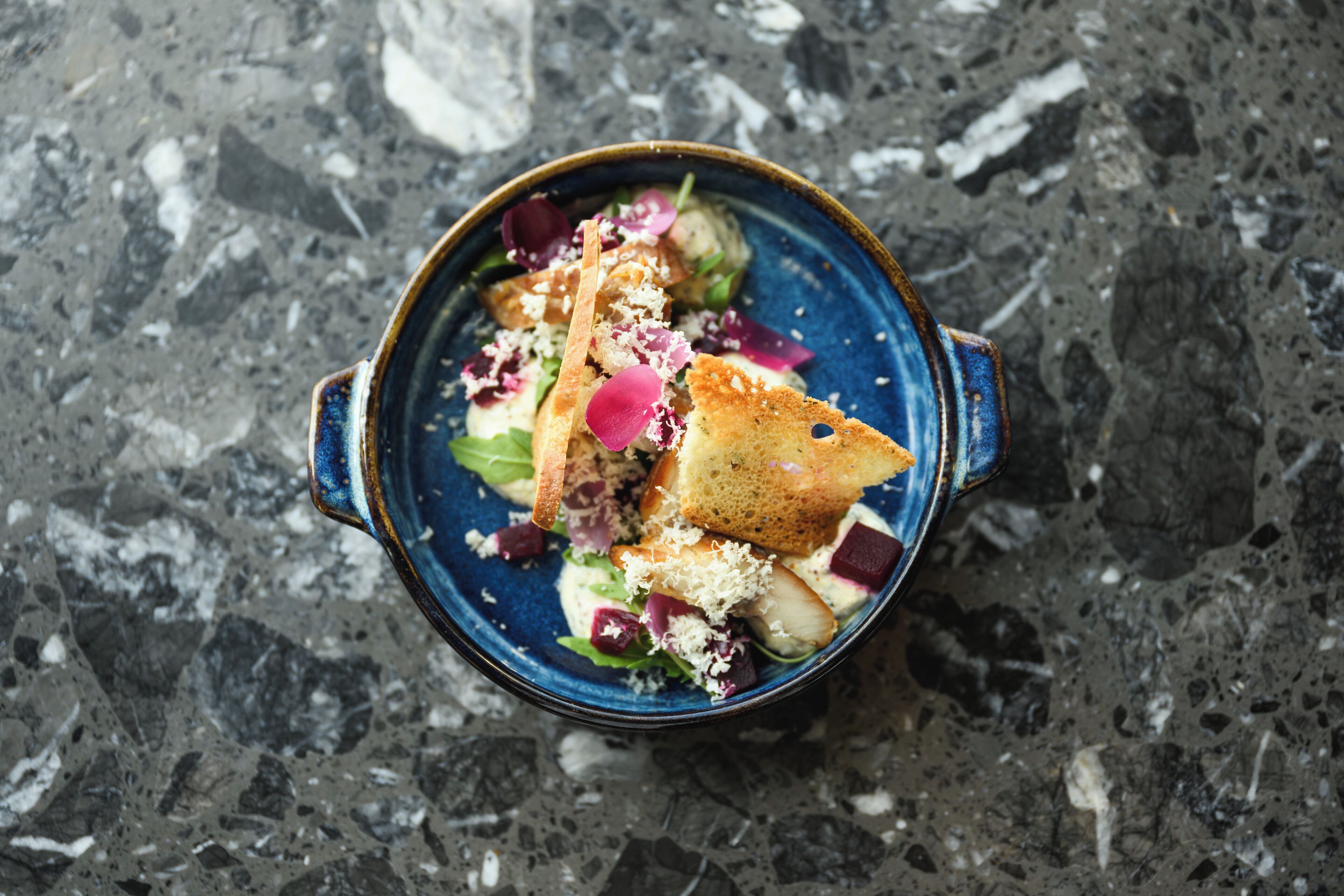 A bowl of salad with croutons and a creamy dressing on a textured surface.