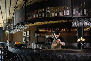 A bar area with a bartender preparing a drink, shelves of liquor bottles, and hanging glasses.