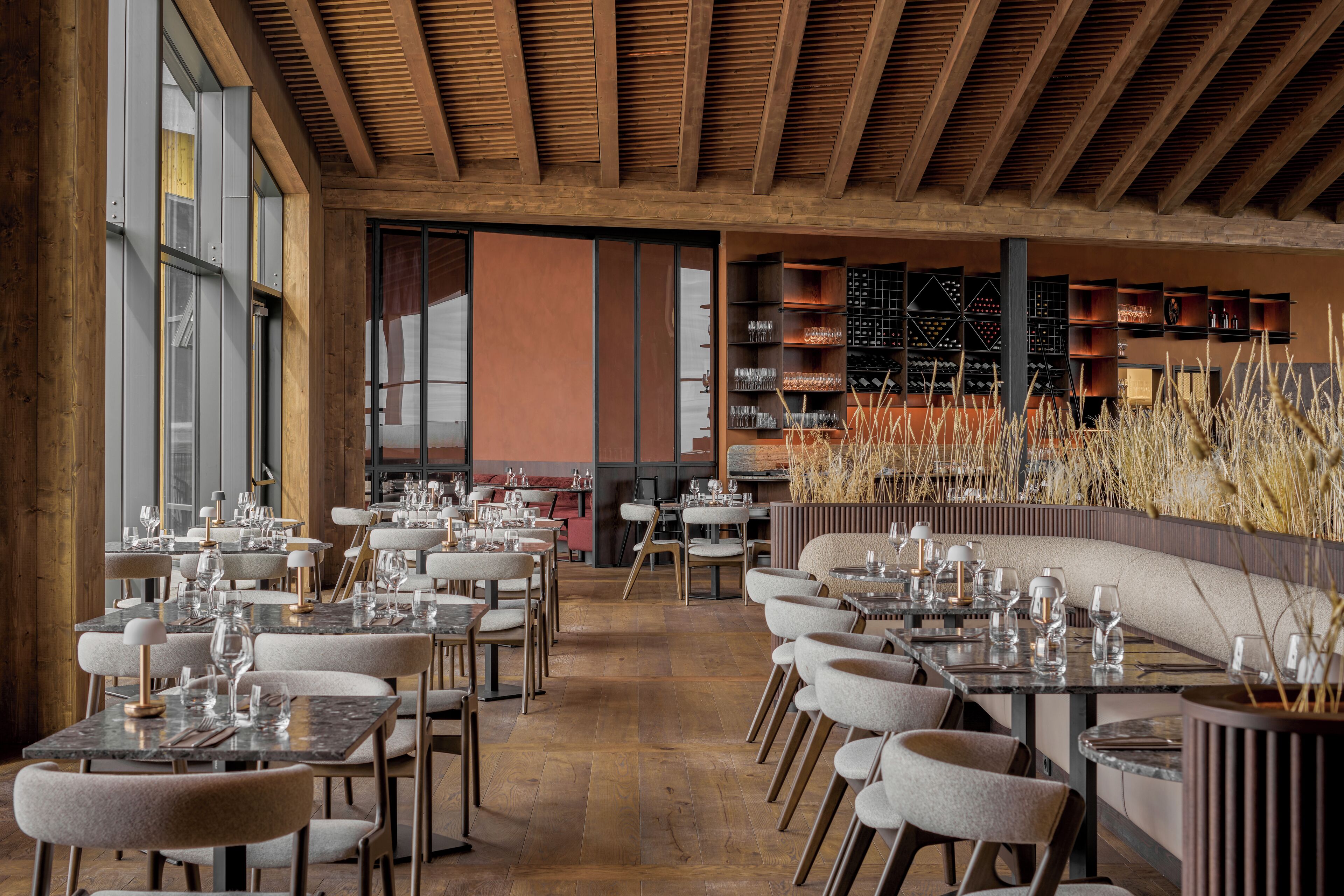 A restaurant interior with wooden beams, tables set with glasses and cutlery, and a wine rack in the background.