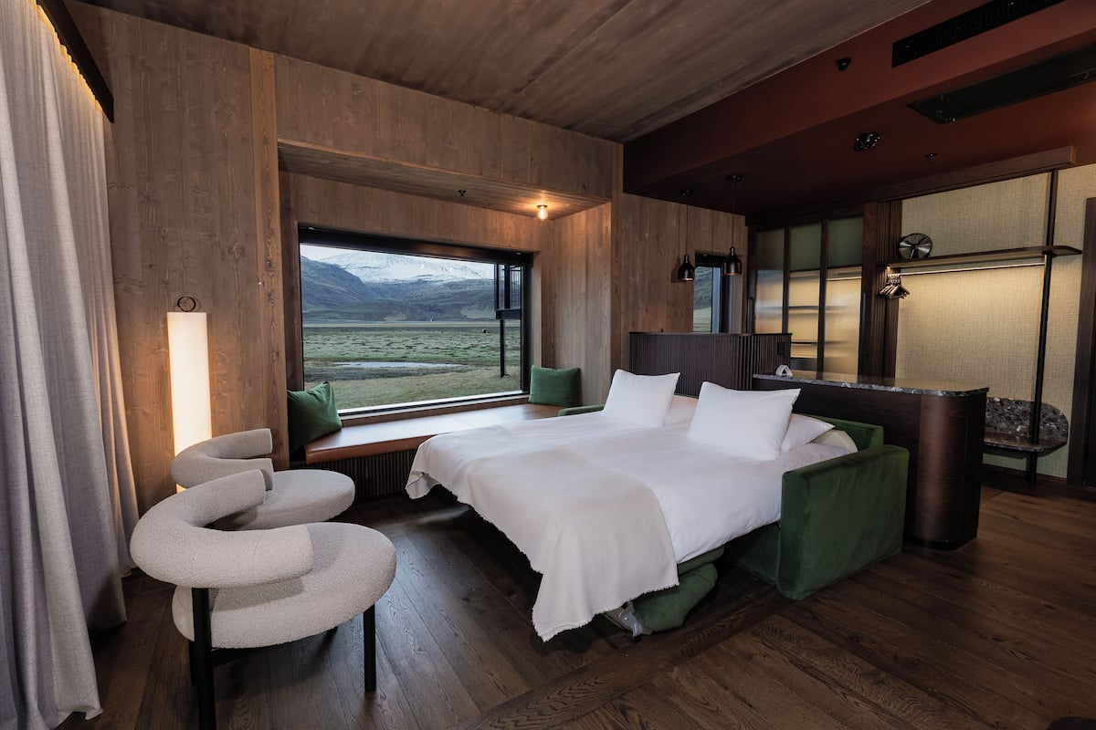 A modern bedroom with a large bed, a curved chair, and a view of a snowy landscape through a window.