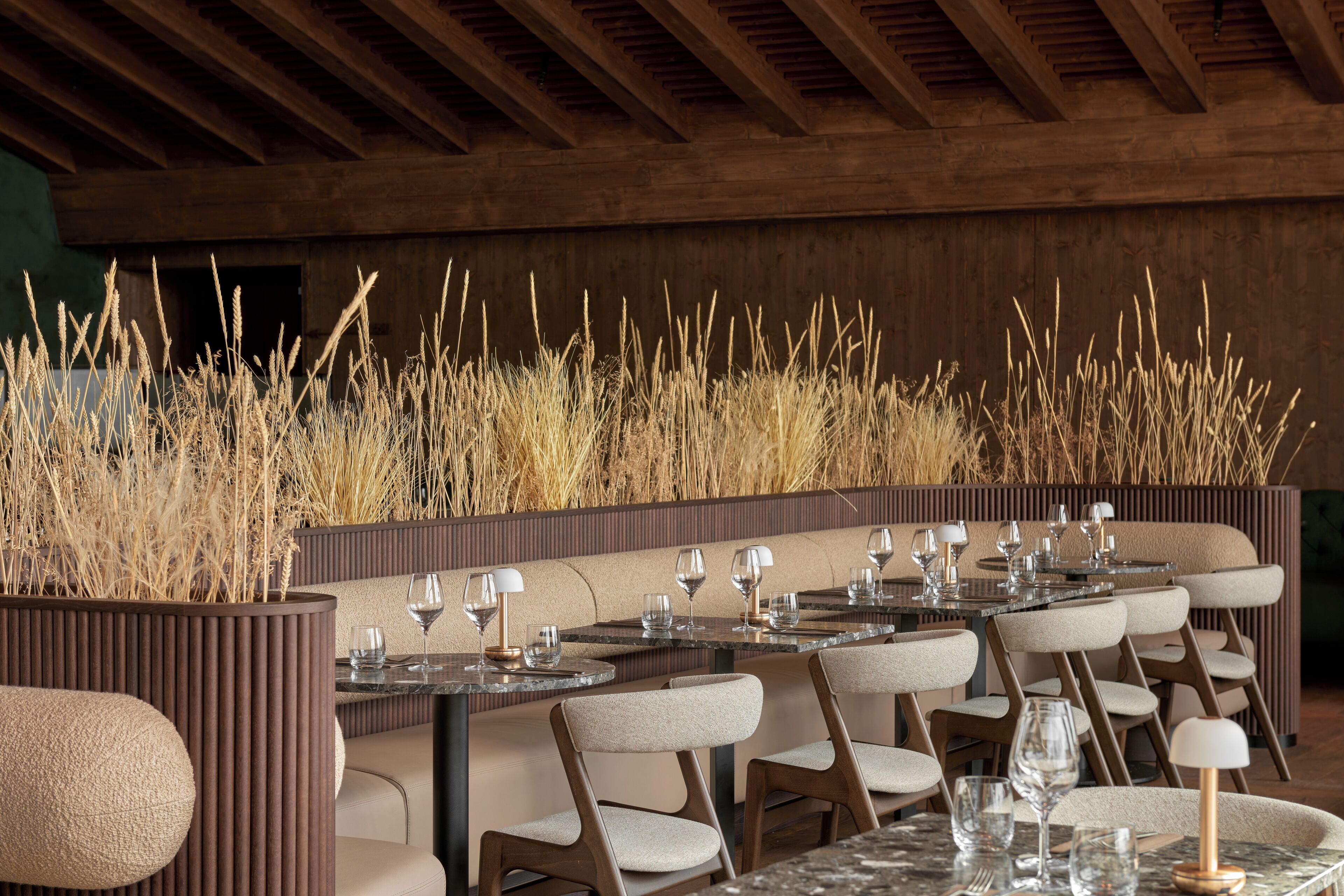 Un restaurant avec des tables rondes, des chaises rembourrées et de hautes herbes en arrière-plan.