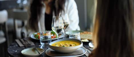 Una mesa de comedor con un tazón de sopa, un plato, un tenedor, un cuchillo y un vaso de agua.